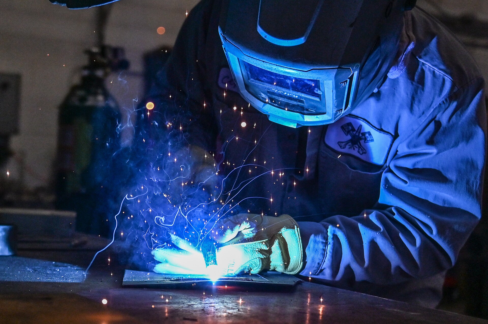 Schweißer mit Schutzschirm setzt einen Lichtbogen an einem Metallteil an.